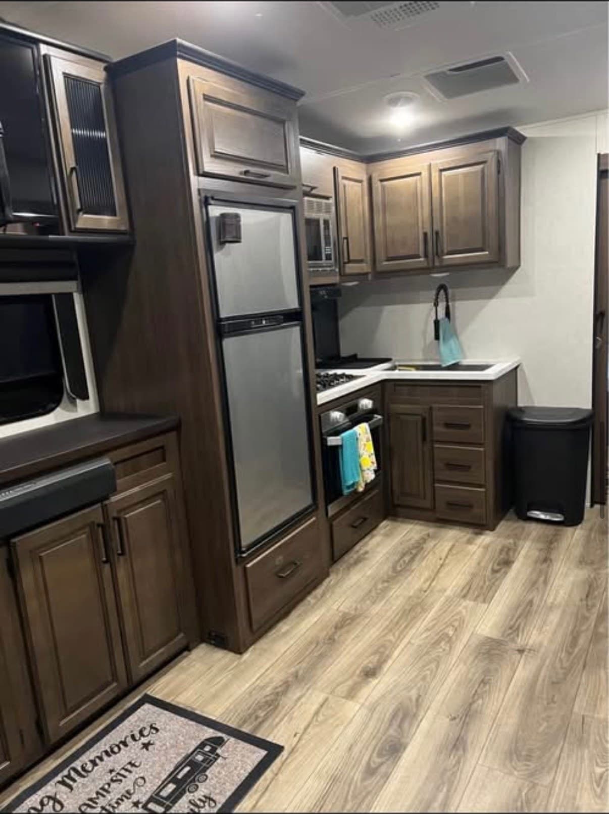 The kitchen in The Crusader with a tall two-door refrigerator, a gas cooktop above a full oven, an overhead microwave, a deep sink and dark wood cabinets
