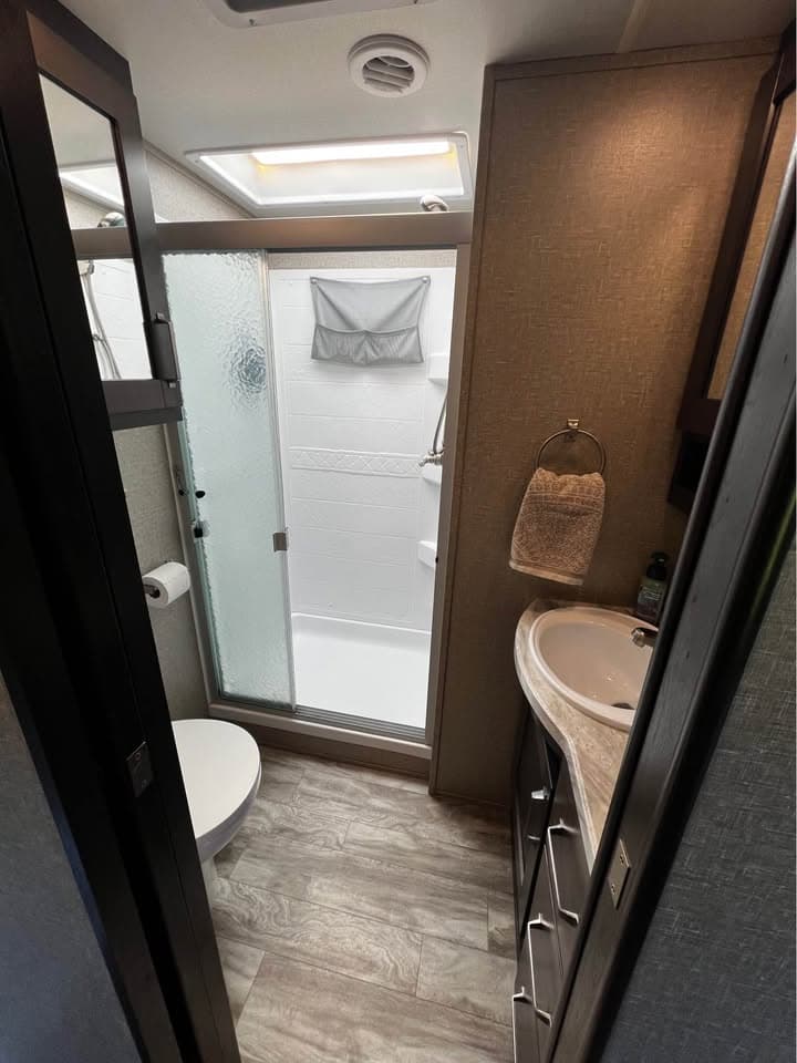 The bathroom in The Reflection with a glass-door shower lit by a skylight, a corner vanity sink and a toilet