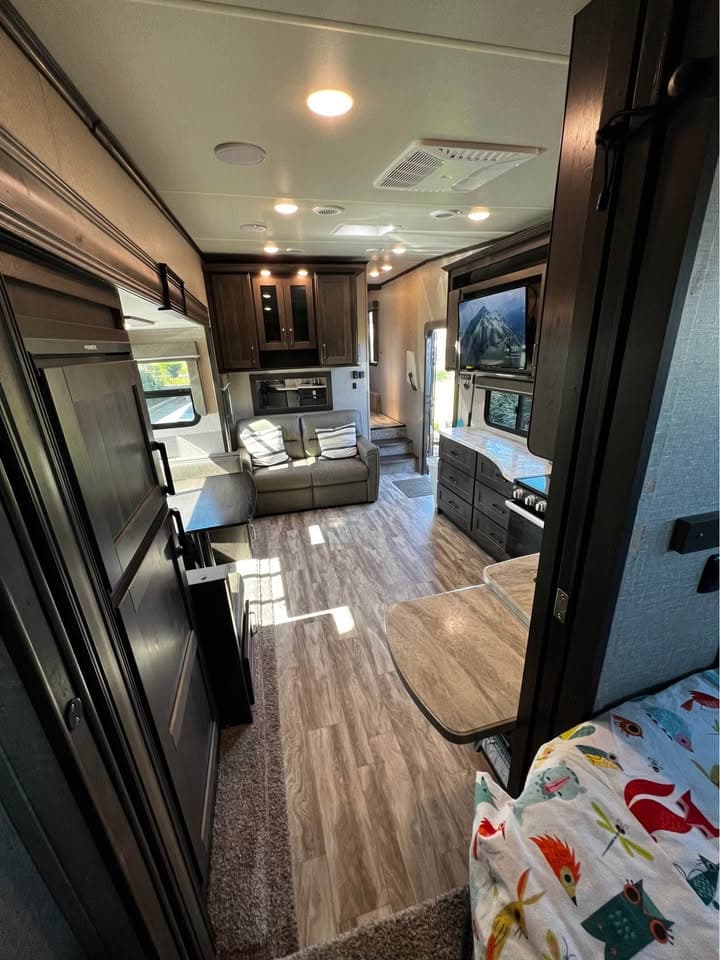 Inside The Reflection looking out from the bunk room toward the tri-fold sofa, the kitchen and the steps up to the front bedroom, with a wall-mounted TV on the right