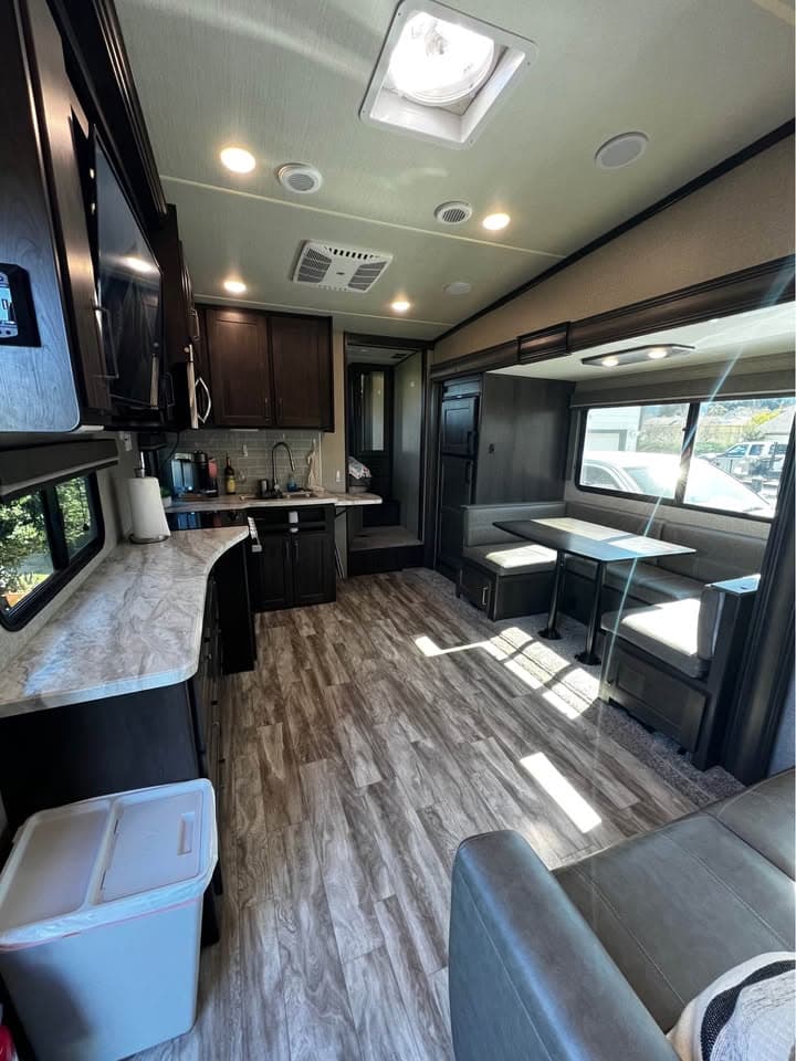 The living area of The Reflection looking toward the kitchen, with the U-shaped dinette in the slide-out under a window, a long counter down the opposite side, and a skylight over the galley